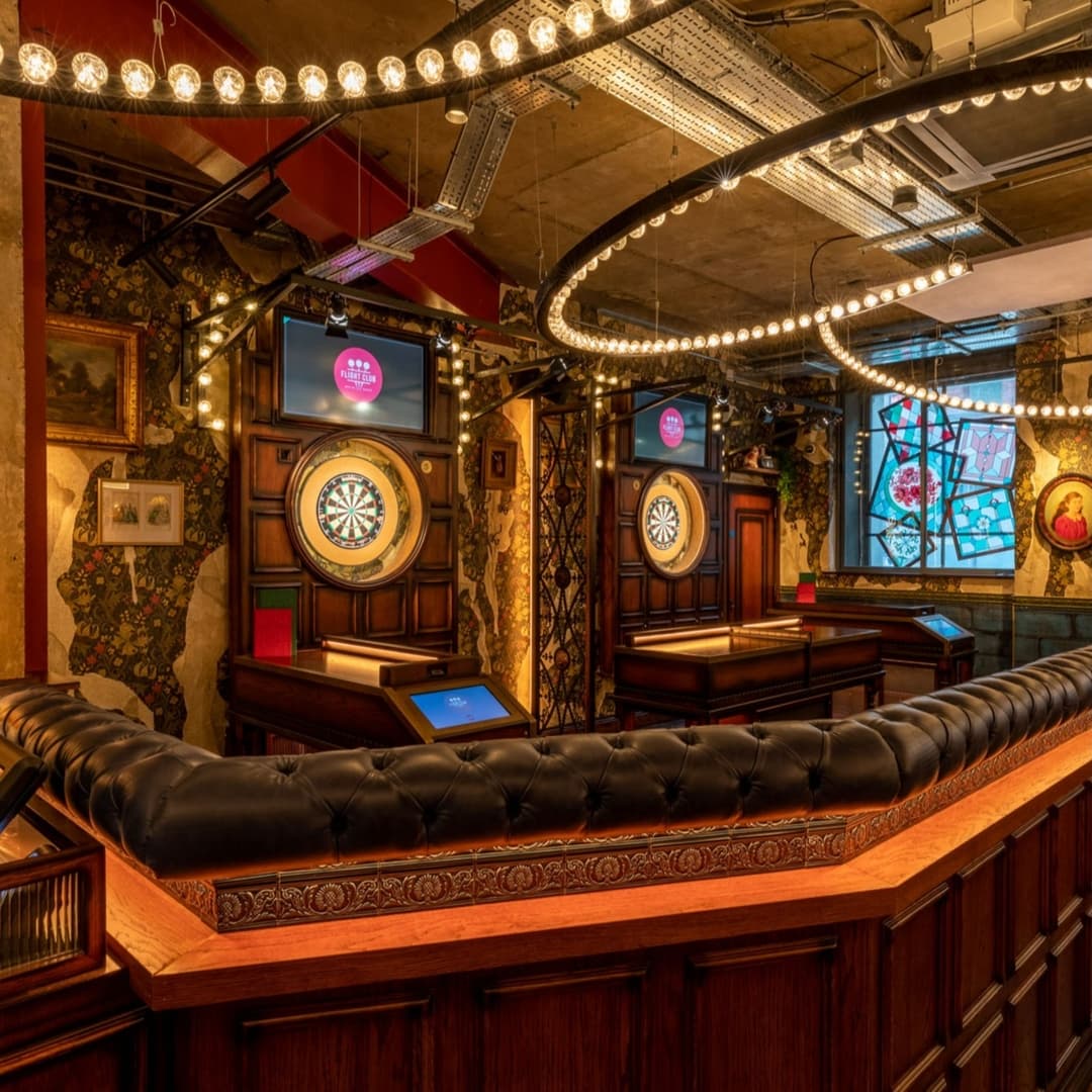 Elegant darts lounge with vintage decor, illuminated by warm lights and featuring dartboards and plush seating.