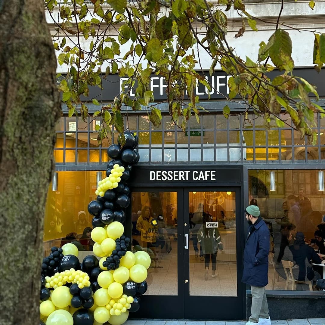 Brightly colored balloons in black and yellow frame the entrance of Fluffy Fluffy Leeds, a bustling dessert café.