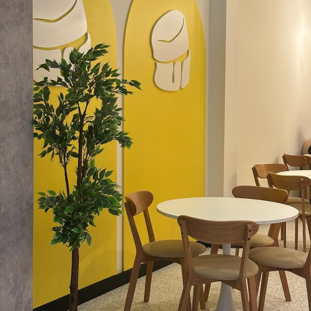 Bright yellow wall with ice cream motifs, a small table with wooden chairs, and a potted plant creating a cozy atmosphere.