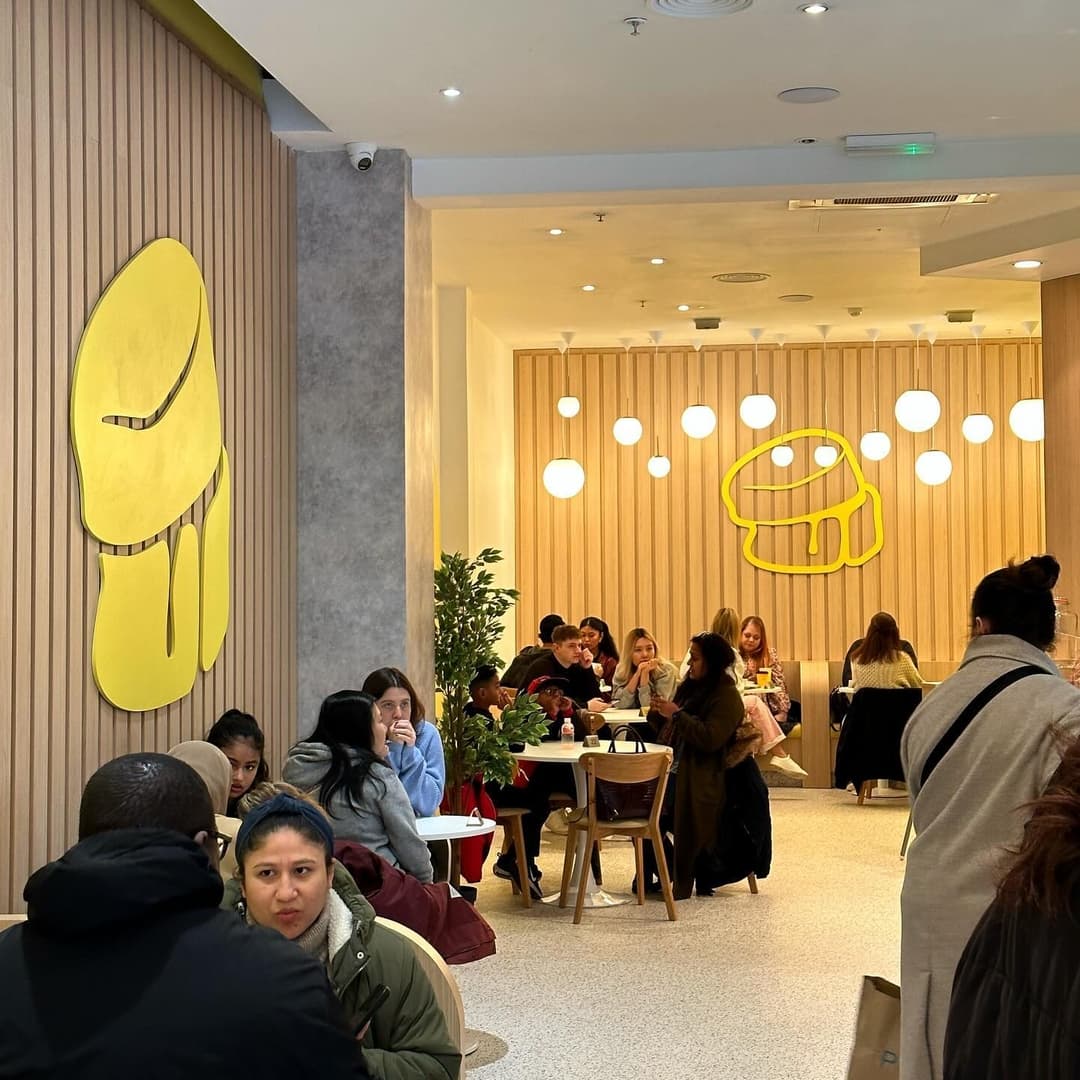 Bright, modern café with yellow decor, cozy seating, and groups enjoying food and drinks in a lively atmosphere.