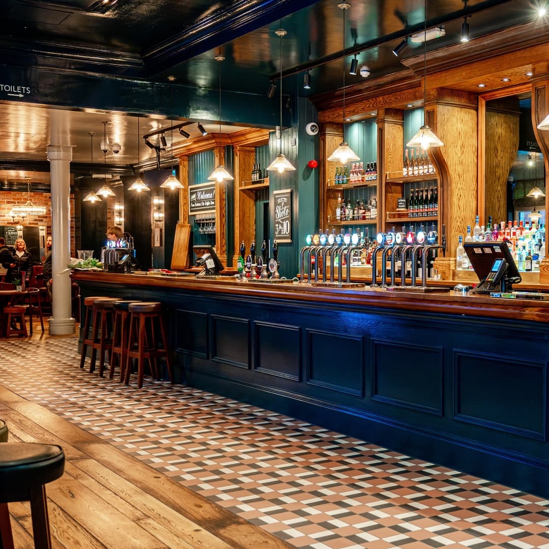 Stylish bar with wooden counters, vintage decor, and patterned tile flooring, creating a warm, inviting atmosphere.