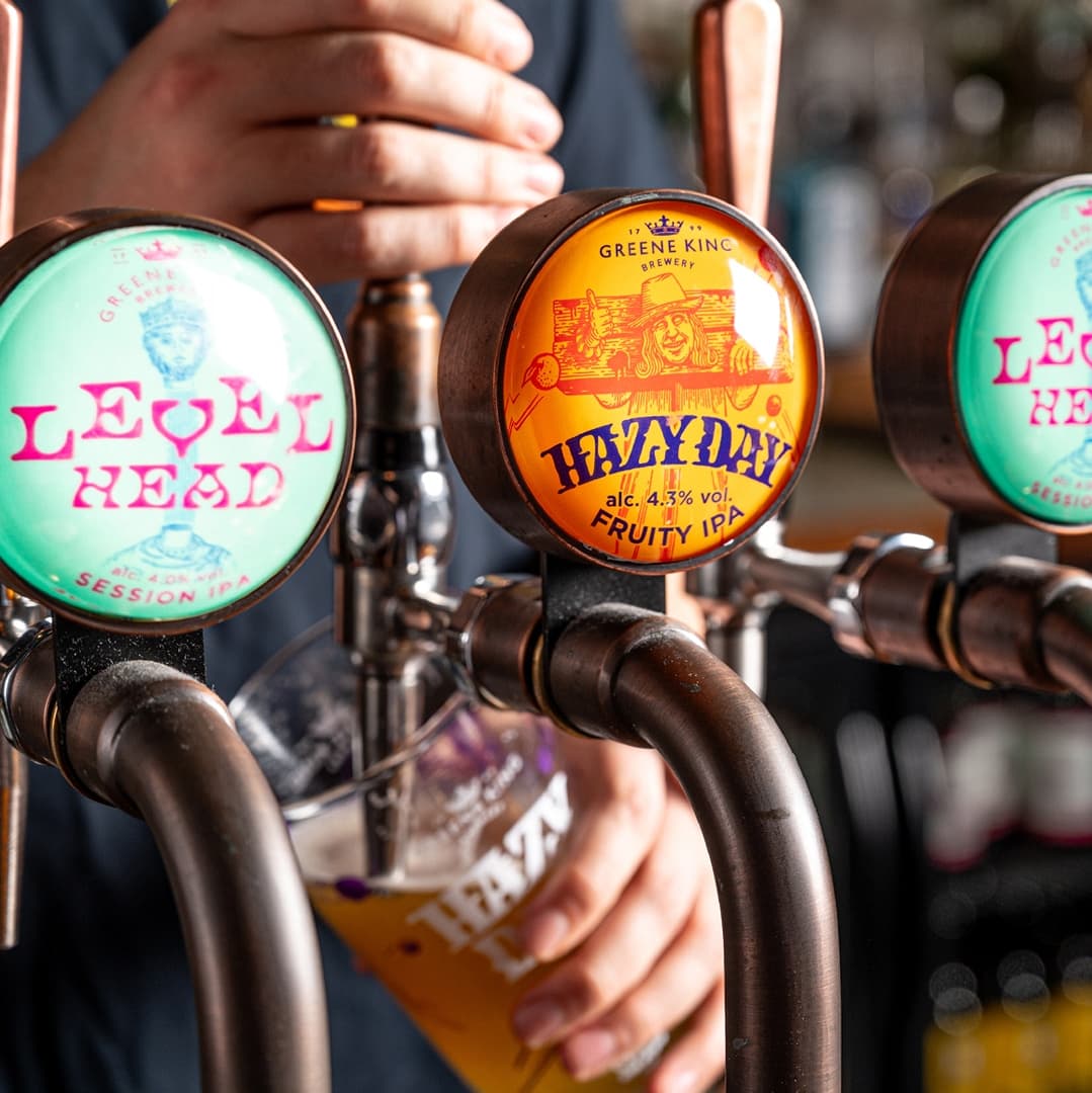 Colorful beer taps with vibrant labels, a hand pouring a golden beer into a glass, creating a lively pub atmosphere.