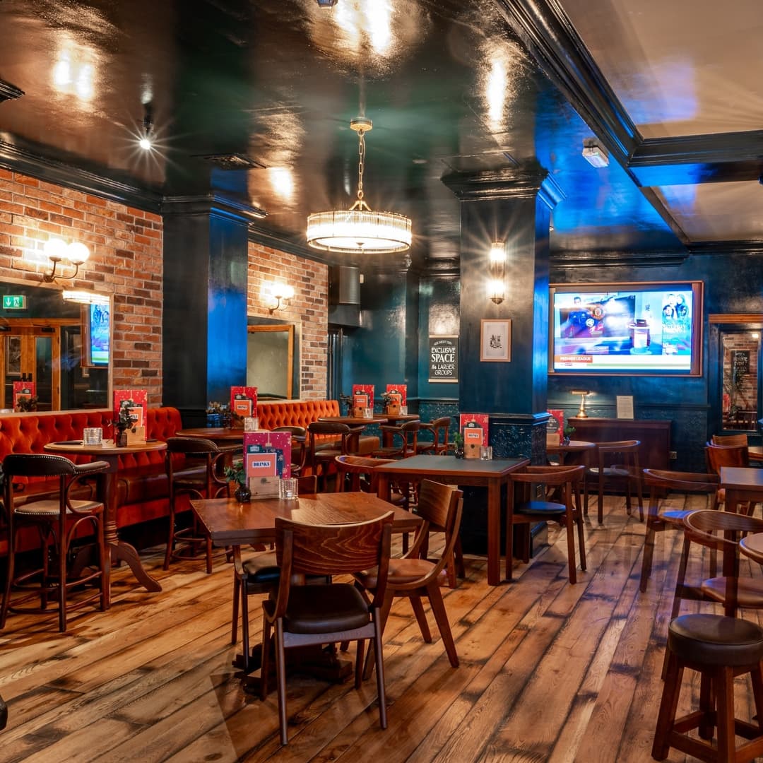 Cozy dining area with wooden floors, red tufted booths, and warm lighting, featuring a TV and rustic decor.