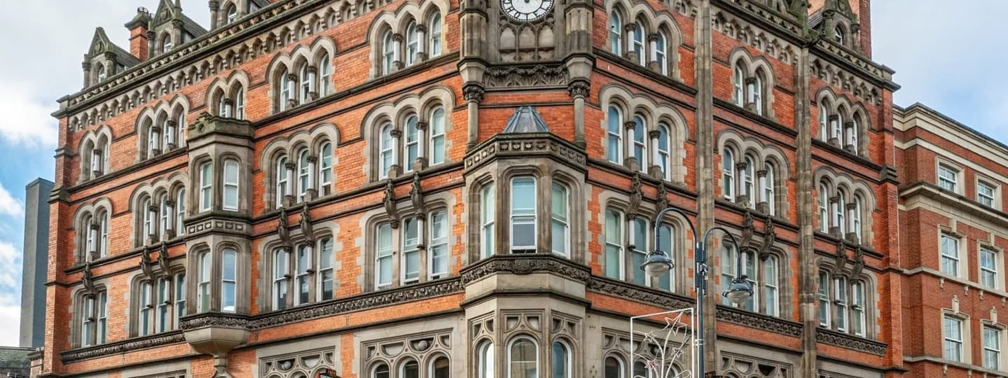 Historic red brick building with ornate architecture, large windows, and a clock tower, set against a blue sky.