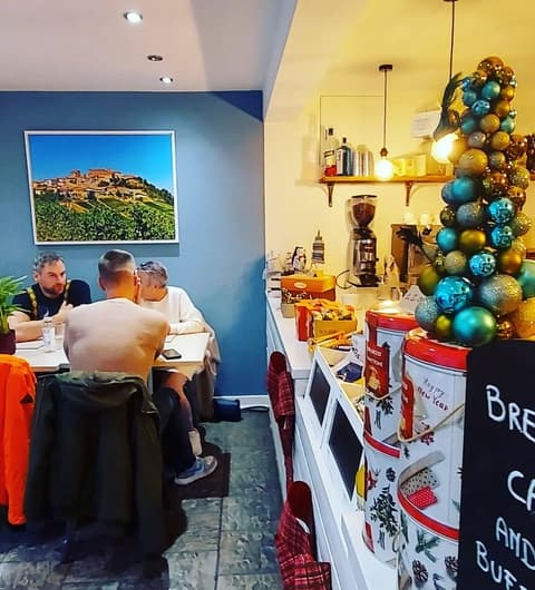 Cozy dining area with patrons at a table, colorful decor, and a festive display of ornaments and coffee equipment.