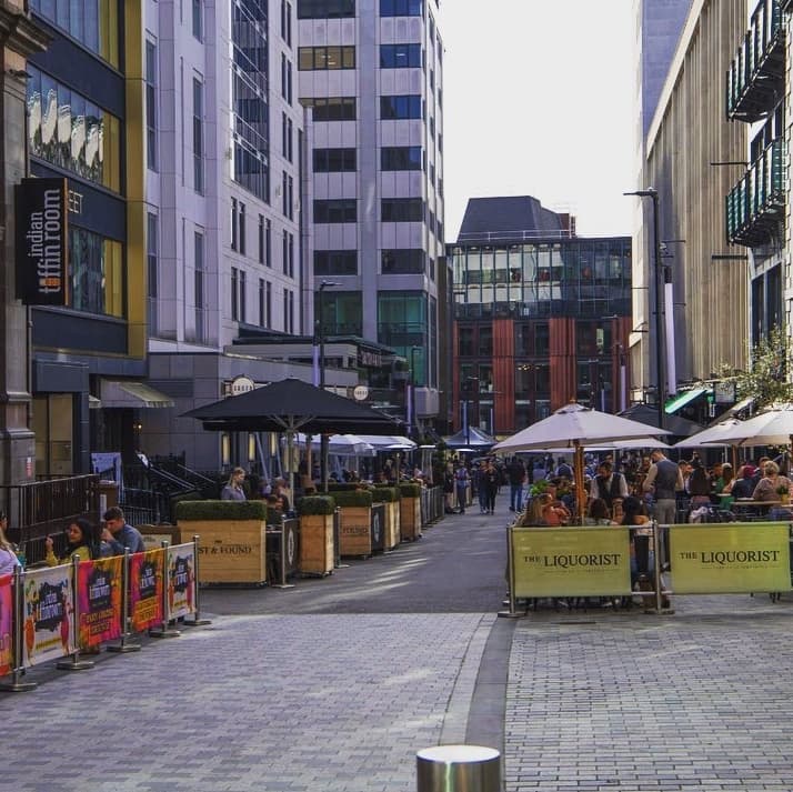 Lively street scene with outdoor dining at Lost & Found, featuring umbrellas, planters, and bustling patrons.