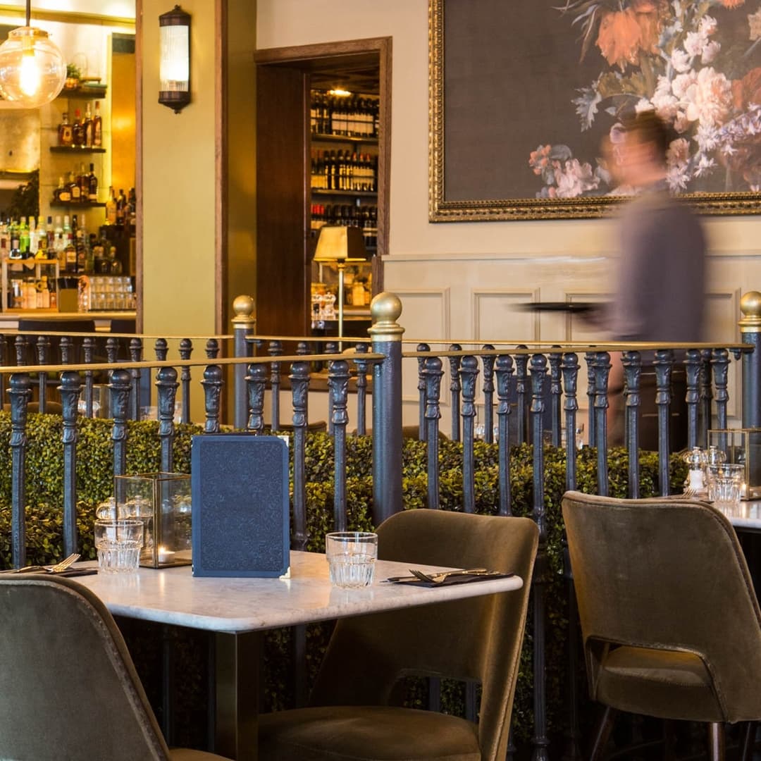 Elegant dining area with marble tables, plush chairs, and a bar in the background, creating a warm, inviting atmosphere.