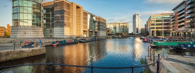 Serene waters reflect modern buildings and boats along the canal, creating a vibrant urban atmosphere in Leeds.
