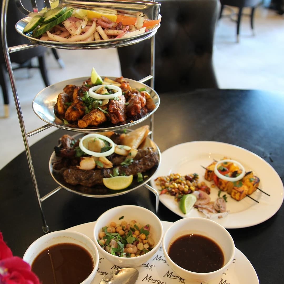 A tiered platter of grilled meats and vegetables, accompanied by dips and garnishes, set on a stylish black table.