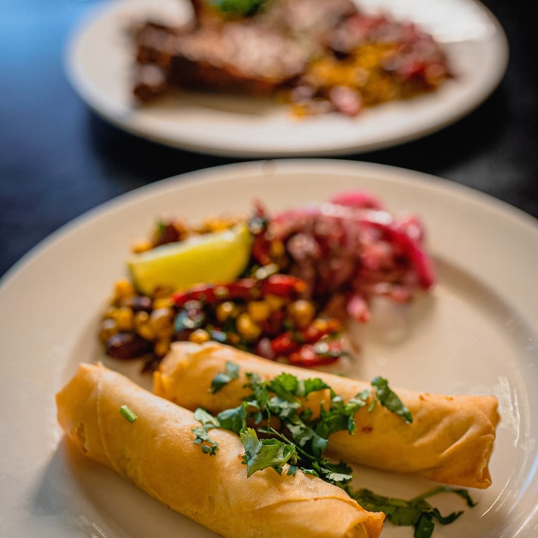 Crispy spring rolls garnished with cilantro, served with a vibrant salad of corn, peppers, and pickled onions.