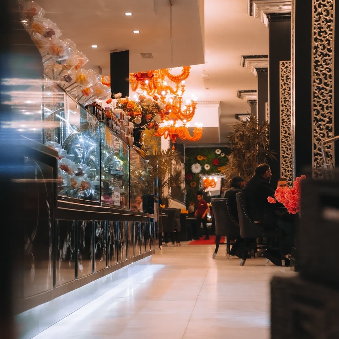 Elegant dining area with ornate decor, vibrant chandeliers, and lush floral arrangements, creating a warm atmosphere.