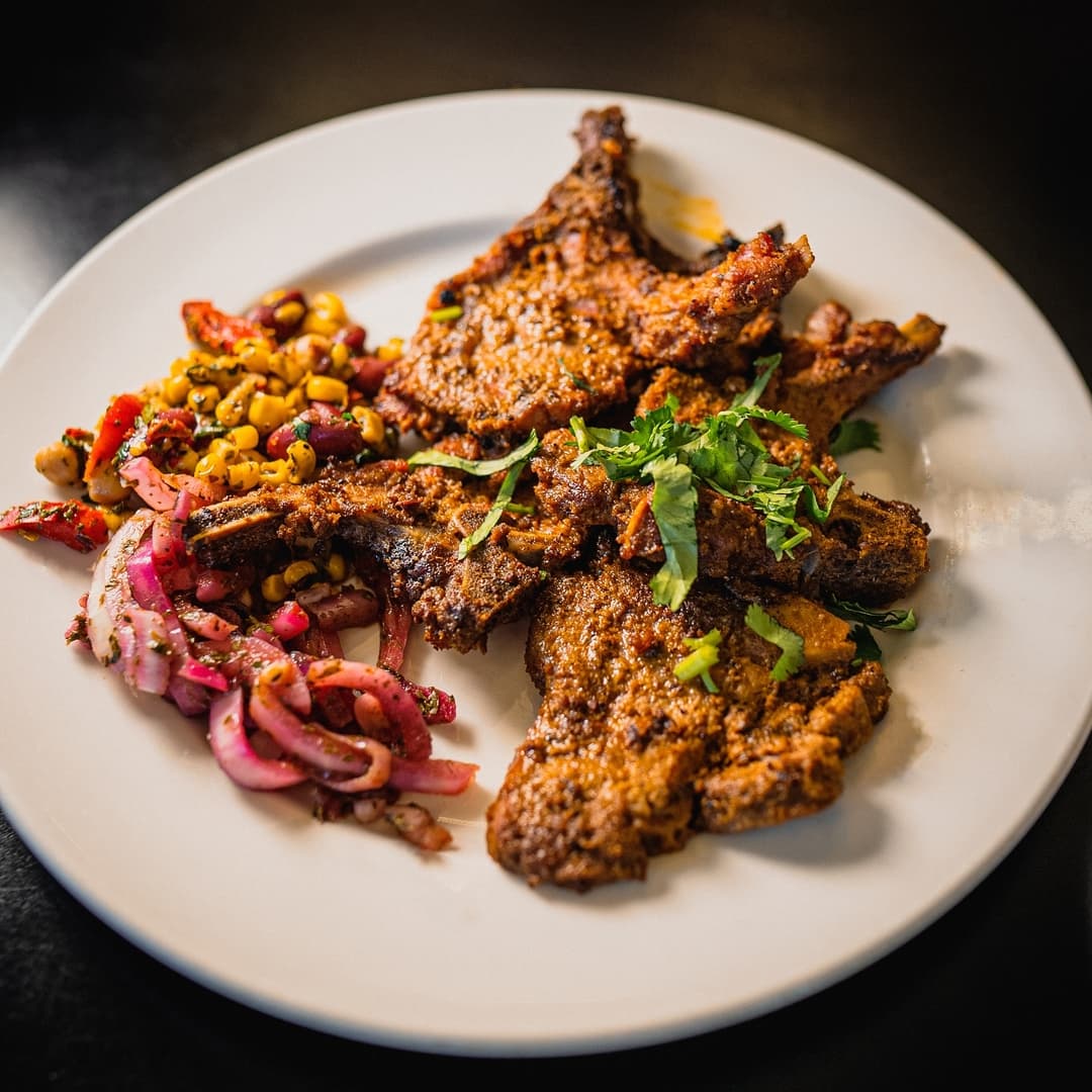Spiced grilled lamb chops garnished with fresh herbs, served with a colorful salad of corn, peppers, and onions.