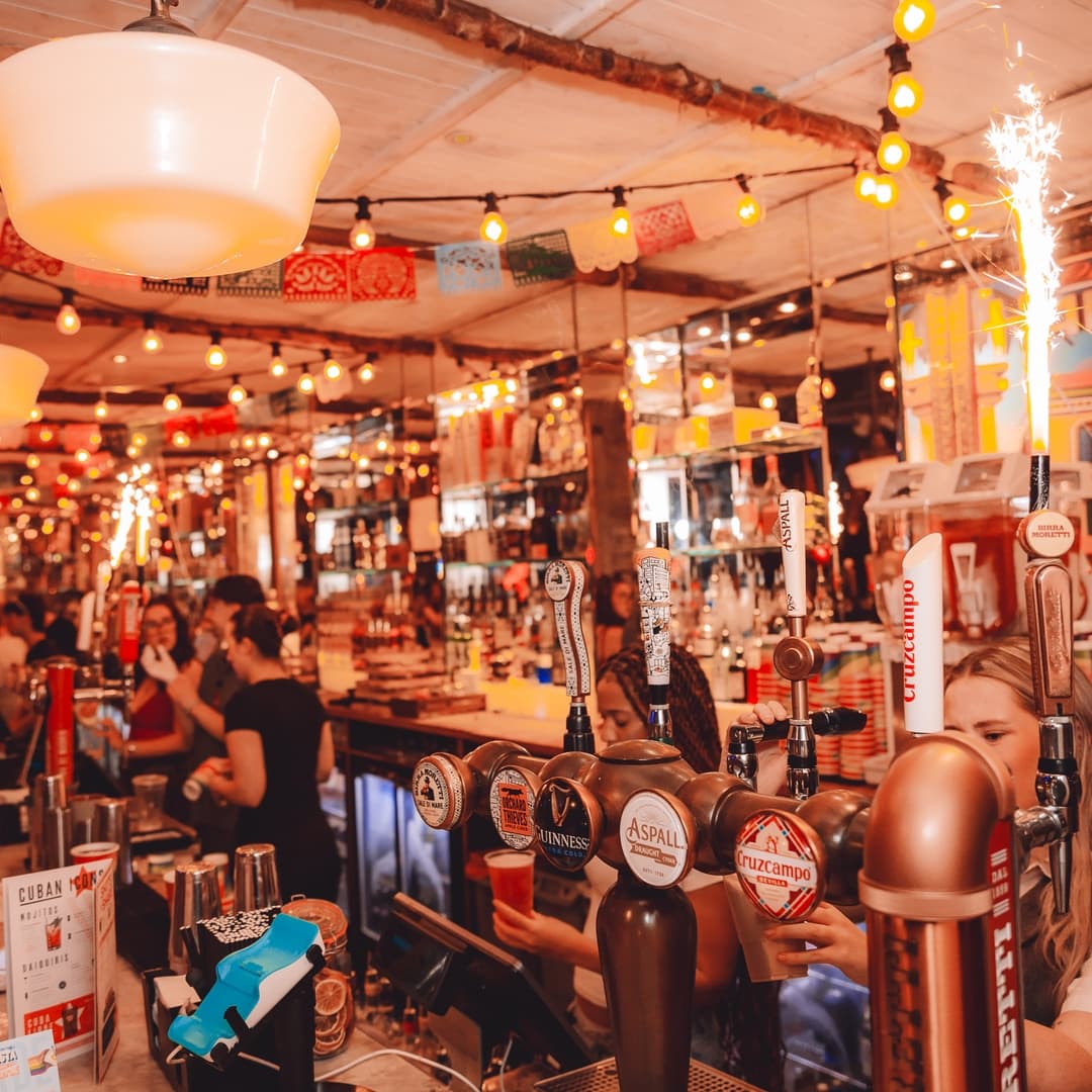 Vibrant bar scene with colorful lights, taps featuring various beers, and a lively atmosphere filled with patrons.