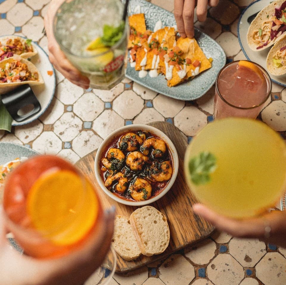 Colorful cocktails and vibrant dishes, including shrimp and nachos, create a lively dining atmosphere at Revolución de Cuba.
