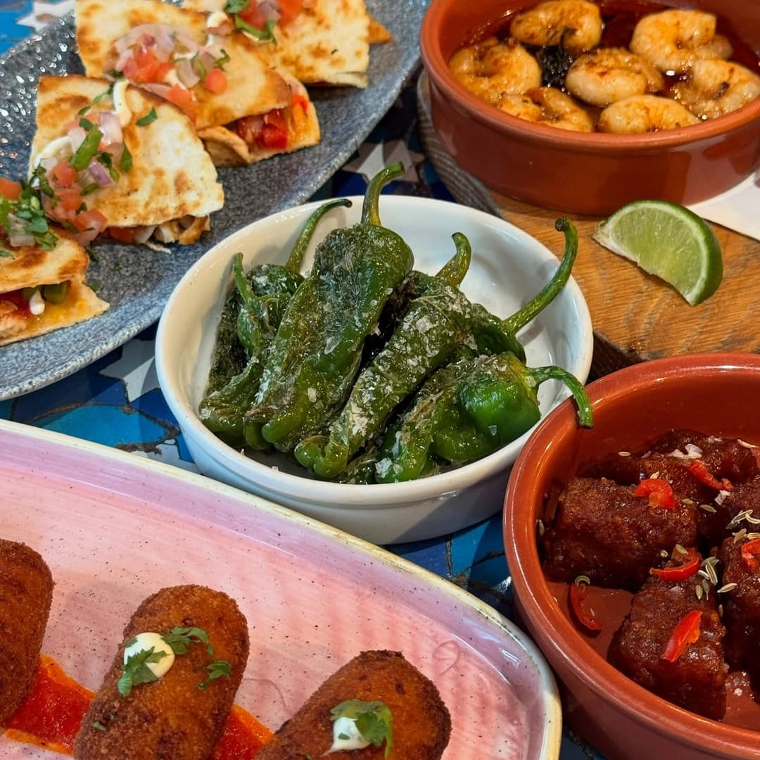Colorful spread of tapas featuring quesadillas, grilled peppers, shrimp, and meatballs, set on a vibrant tiled table.