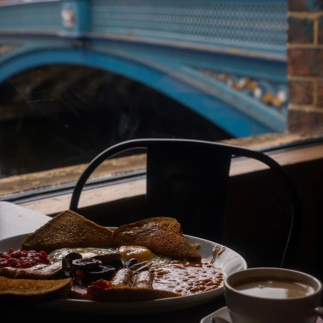 A hearty breakfast plate with toast, eggs, and beans, framed by a view of a blue bridge over a tranquil river.
