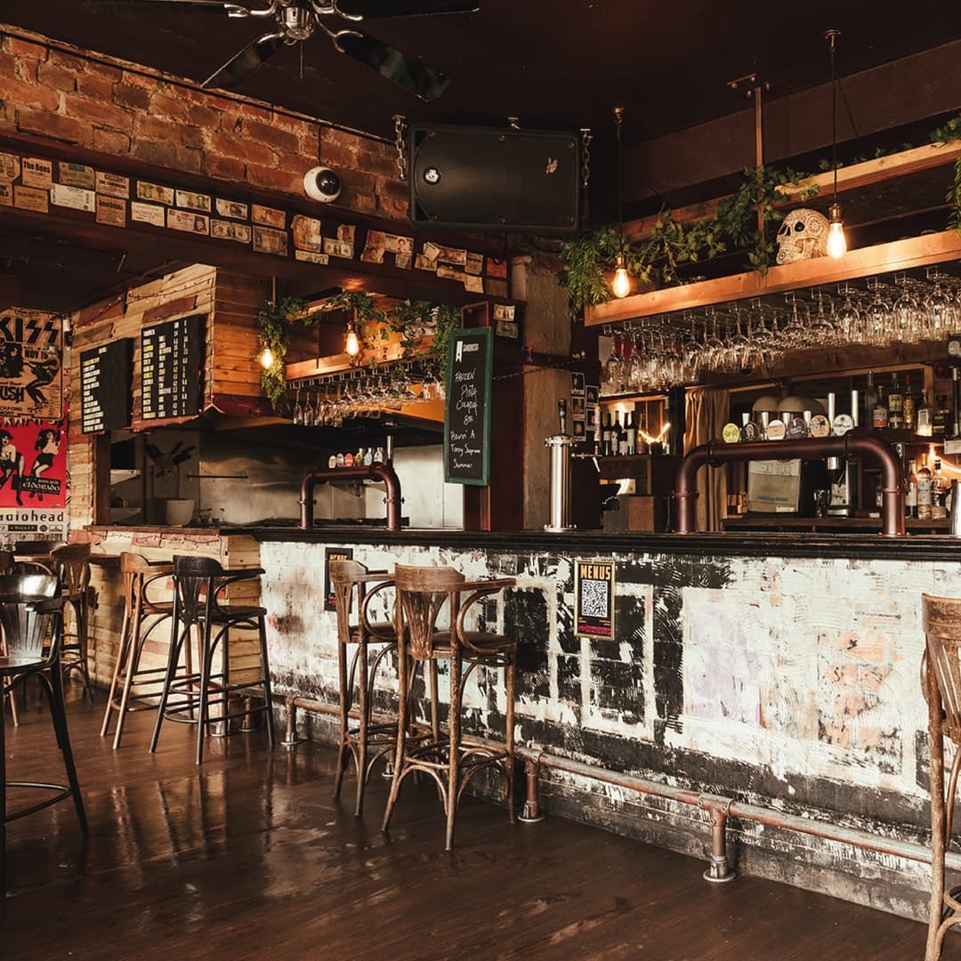 Rustic bar with wooden stools, exposed brick walls, and hanging plants, creating a cozy, vibrant atmosphere.