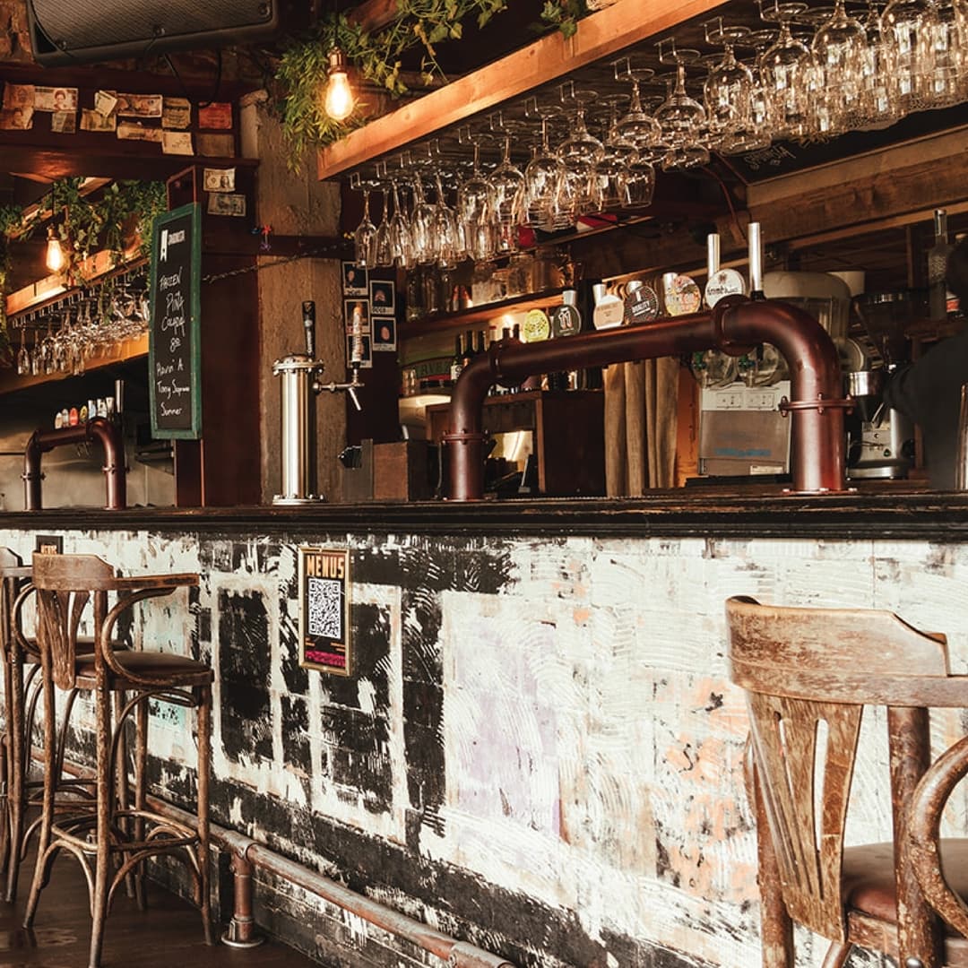 Rustic bar with wooden stools, hanging glassware, and vibrant decor, creating a warm and inviting atmosphere.