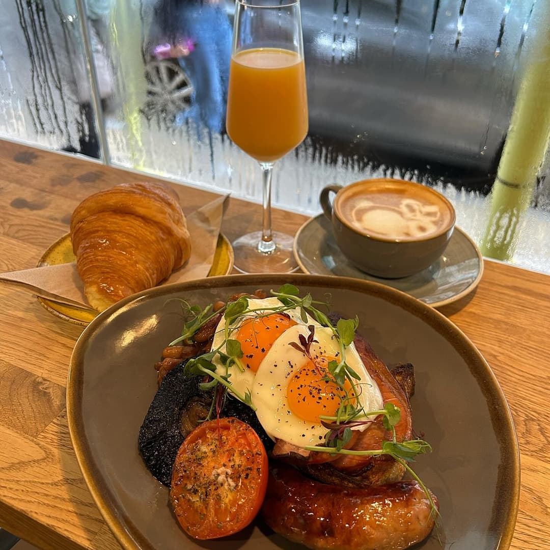 A hearty breakfast plate with eggs, sausage, and tomatoes, paired with a croissant and a glass of orange juice.