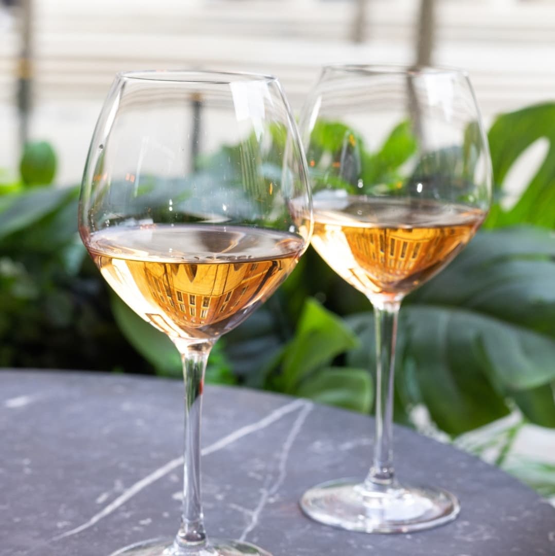 Two elegant wine glasses filled with rosé wine, reflecting greenery and the restaurant's ambiance on a marble table.