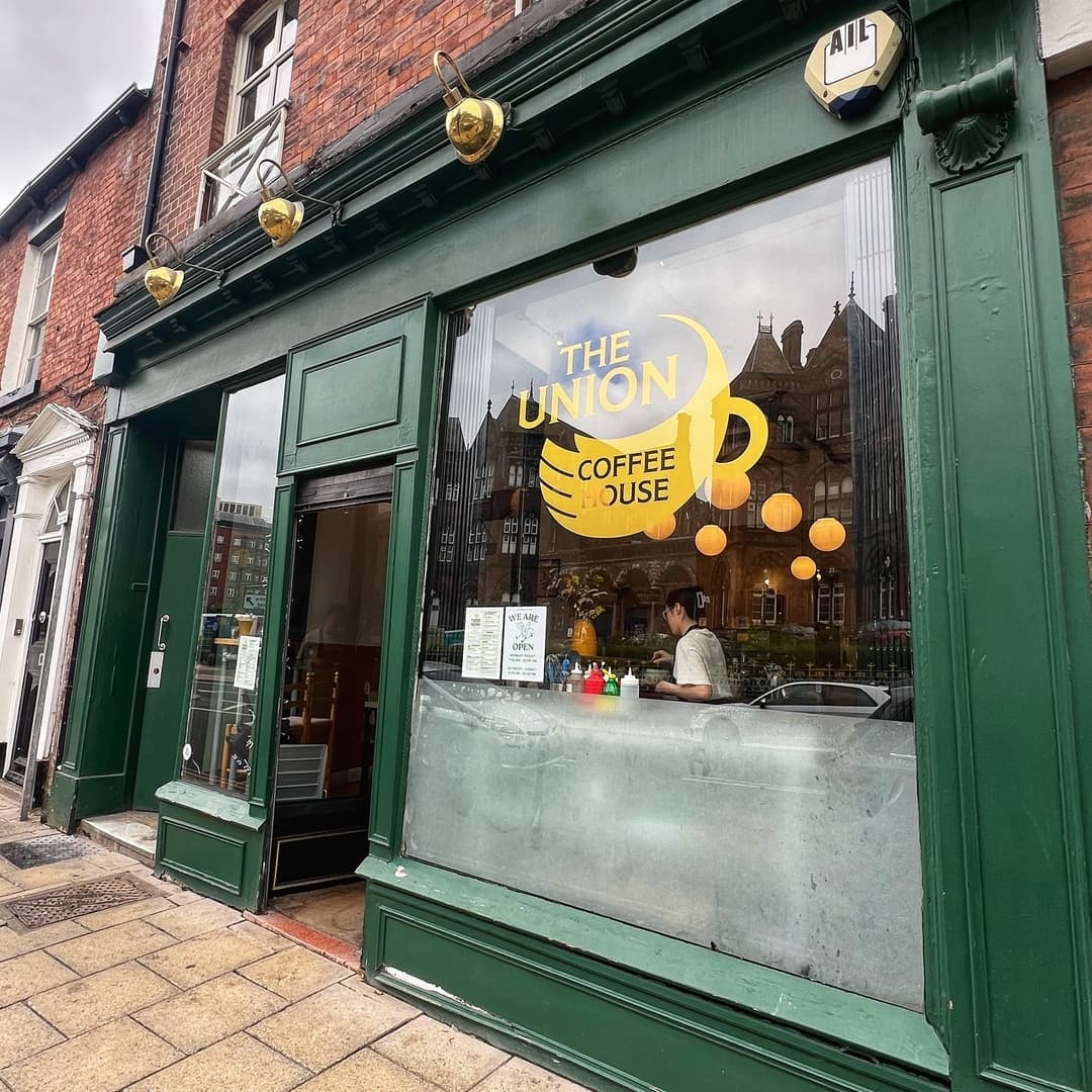 Charming café exterior with large windows, yellow signage, and warm lighting, inviting guests to enjoy coffee and pastries.
