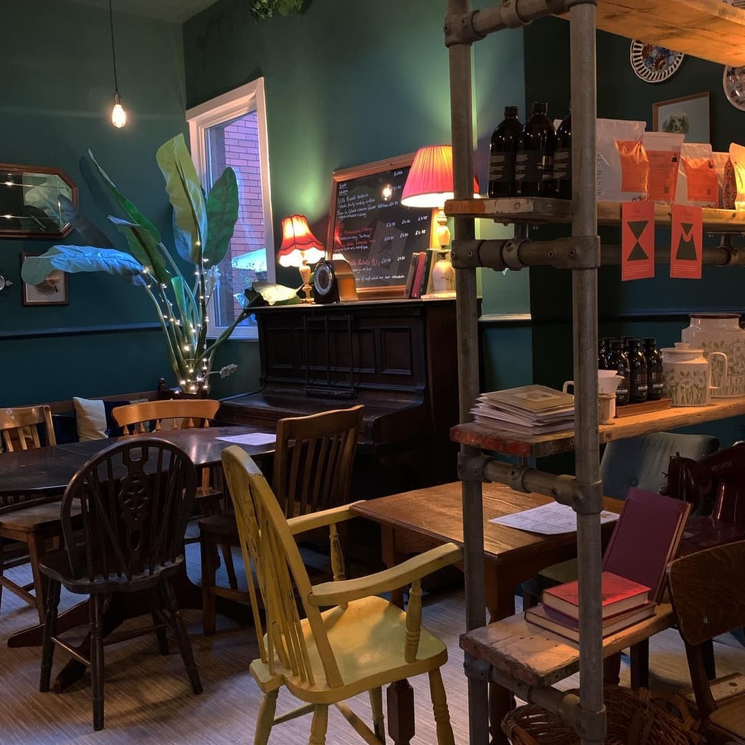 Cozy coffee house with green walls, vintage furniture, warm lighting, and a lively plant, creating a welcoming atmosphere.