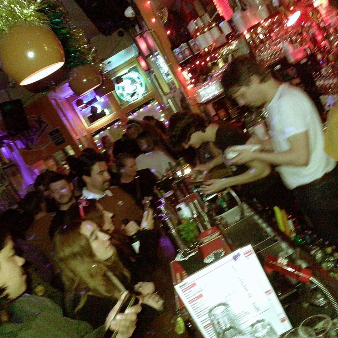 Lively bar scene at Wax Bar with colorful lights, a busy bartender, and patrons enjoying drinks and conversation.