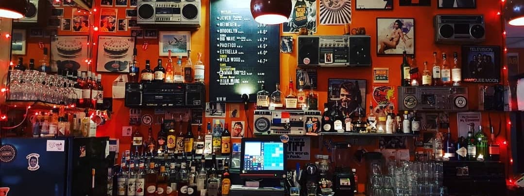 Vibrant bar scene with an orange wall, vintage decor, illuminated bottles, and a chalkboard menu.