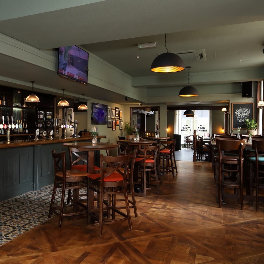 Warm, inviting pub interior with wooden bar, high tables, and soft lighting, creating a cozy dining atmosphere.