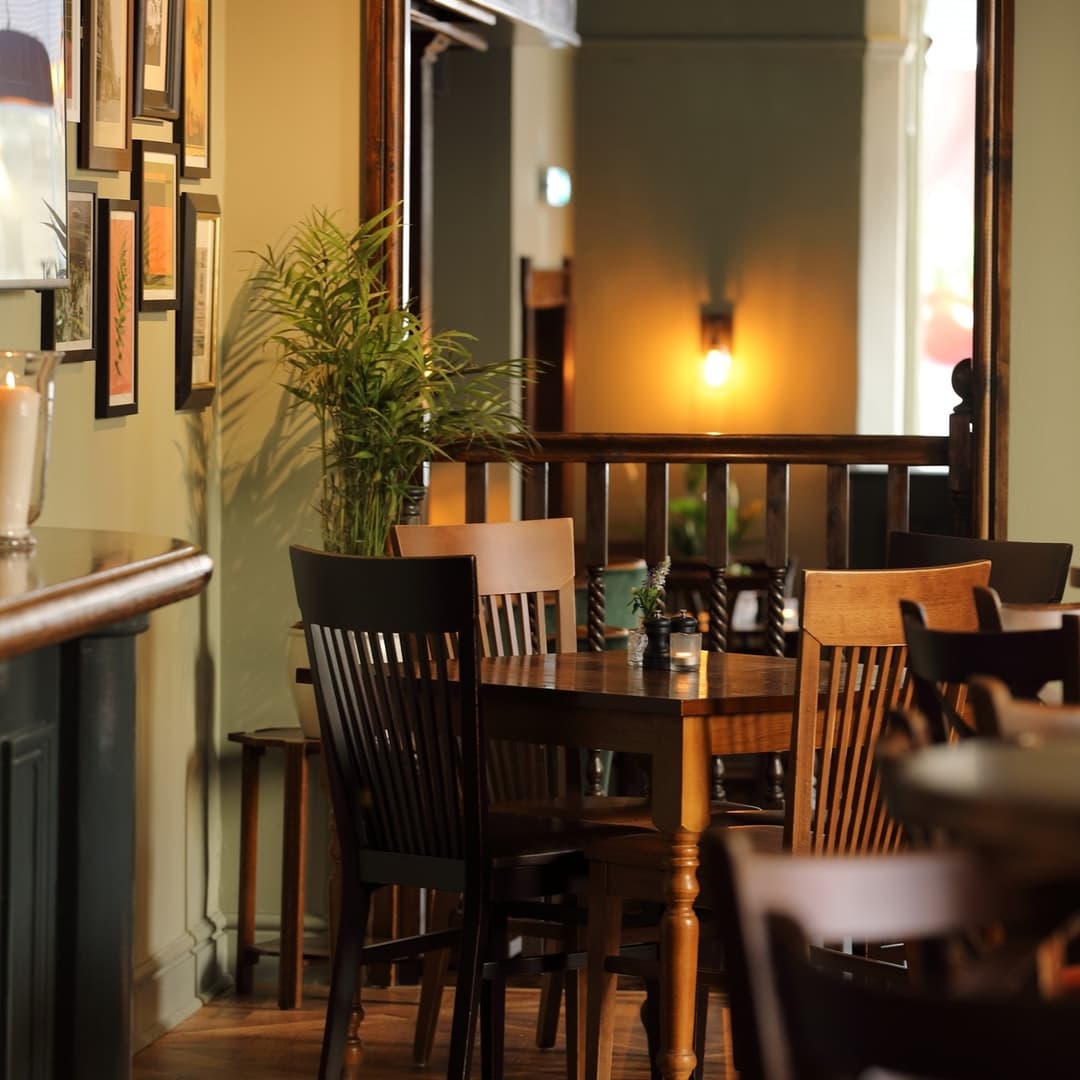 Warm wooden tables and chairs create an inviting atmosphere, complemented by soft lighting and green plants.