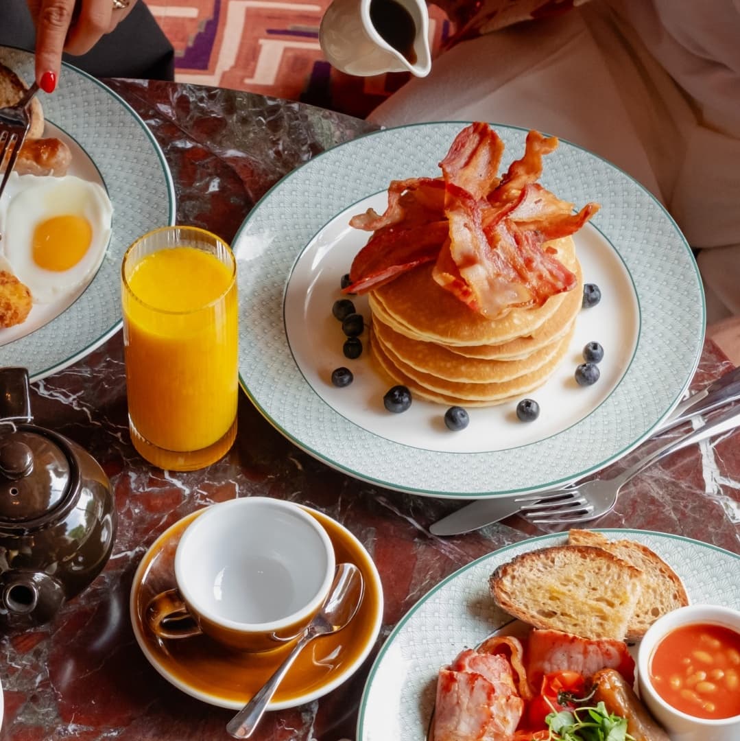 A vibrant brunch spread featuring pancakes topped with bacon, eggs, toast, and fresh juice on a stylish table.