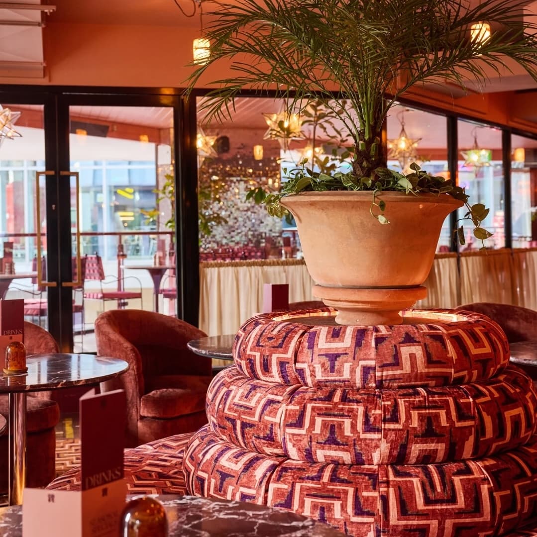 Vibrant Lounge with Artistic Seating Lush potted plant atop a colorful patterned seating area, surrounded by stylish tables and cozy seating in a vibrant dining space.