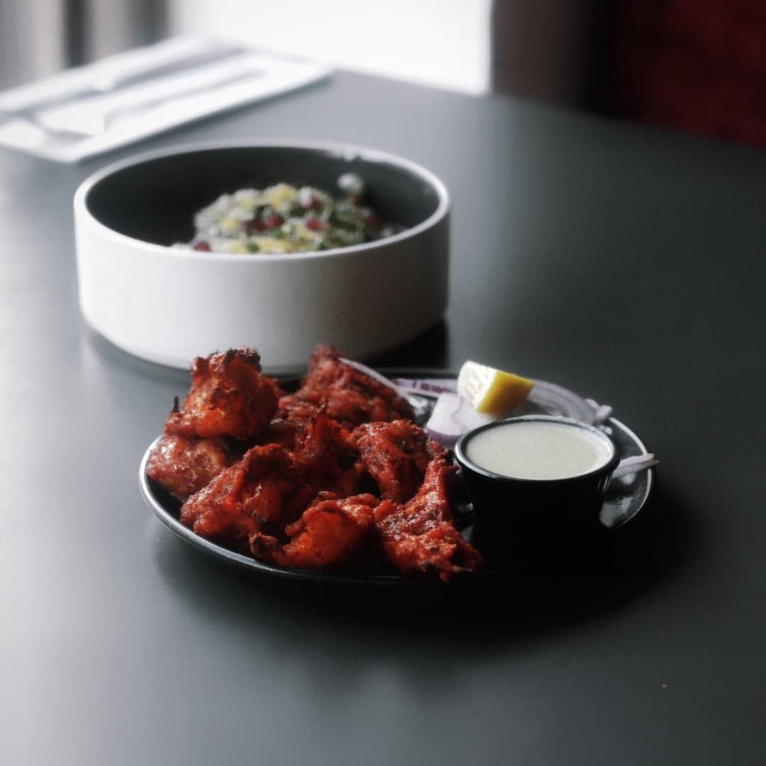 Plate of vibrant, spiced chicken tikka with a lemon wedge and mint sauce, alongside a bowl of colorful salad.