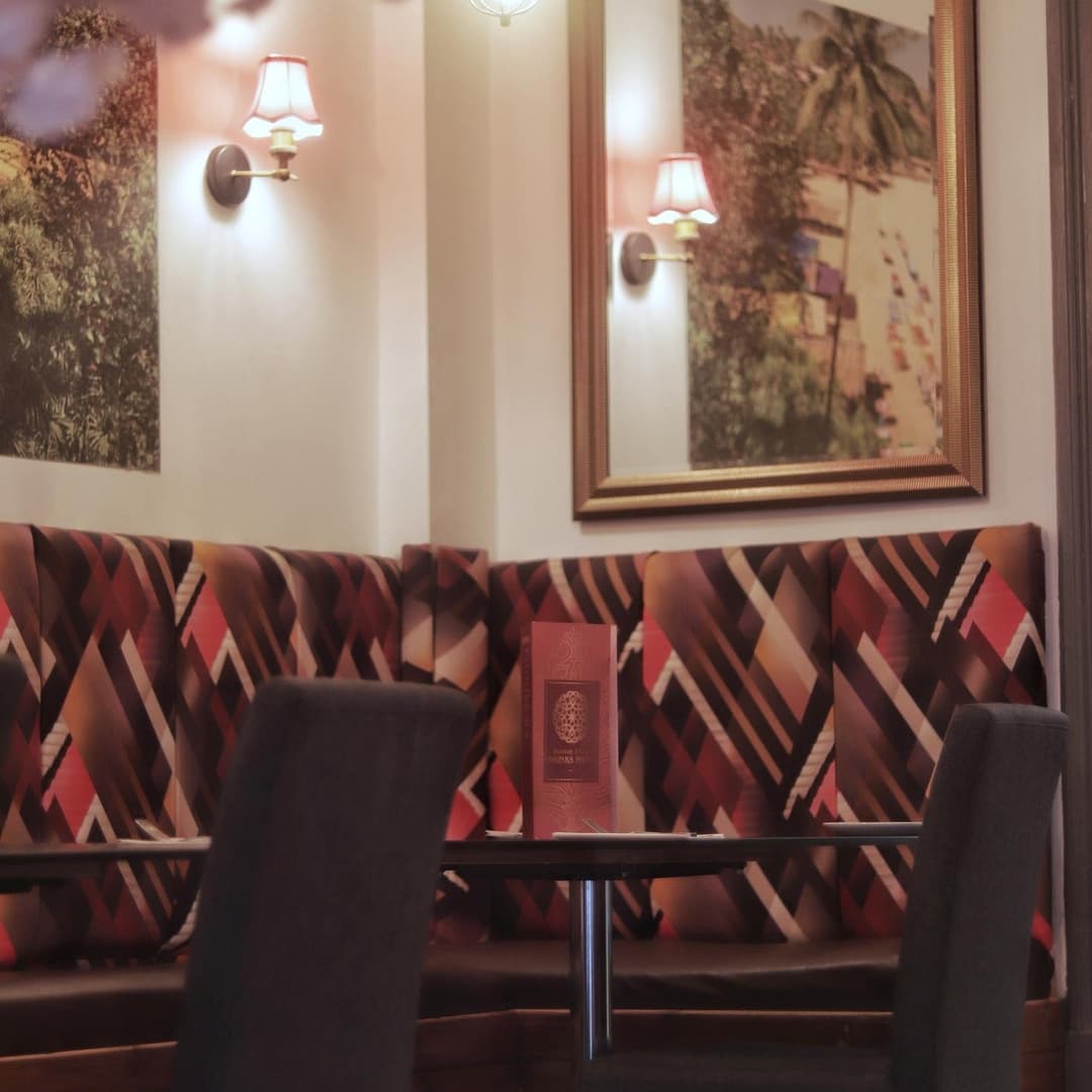 Cozy dining area with patterned booth seating, warm lighting, and vibrant wall art, creating an inviting atmosphere.