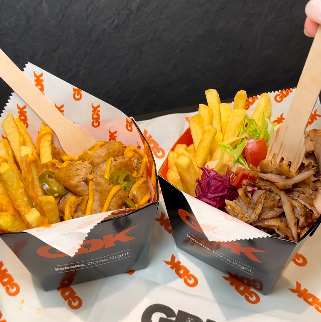Two black takeout boxes from GDK filled with golden fries and flavorful kebab, garnished with fresh vegetables.