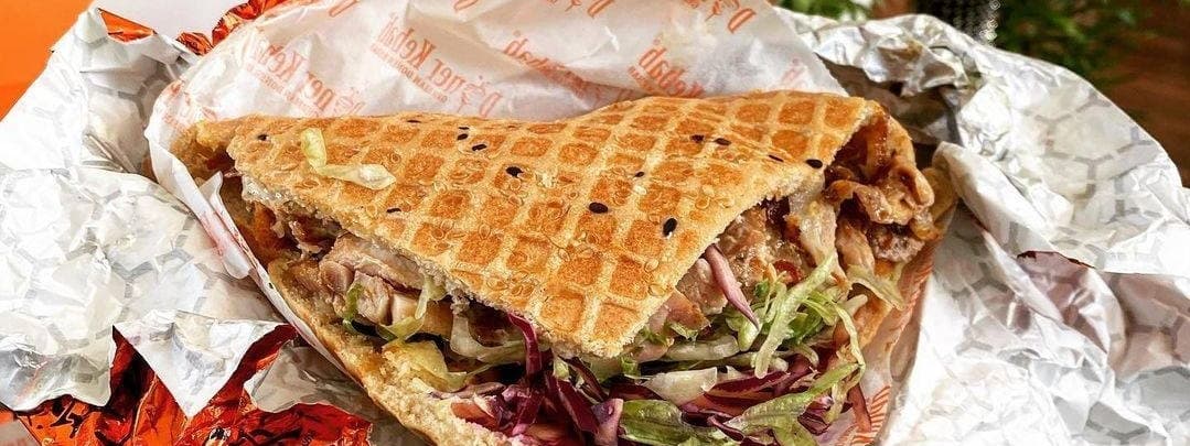 A freshly made German Doner Kebab wrapped in foil, filled with grilled meat, fresh vegetables, and sauces, exuding deliciousness.