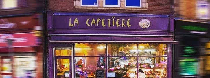 Charming café exterior with purple signage, warm lights, and a cozy atmosphere, inviting guests to enjoy a delightful experience.