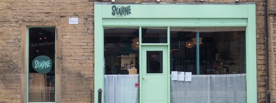 Charming bistro with a mint green facade, large windows, and inviting outdoor seating, set in a rustic stone building.