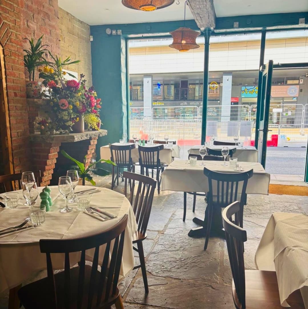 Charming bistro interior with wooden tables, elegant table settings, and a floral display near a large window.