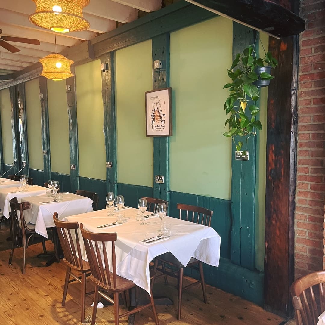 Charming bistro interior with wooden tables, white tablecloths, and green walls, featuring warm pendant lighting and plants.