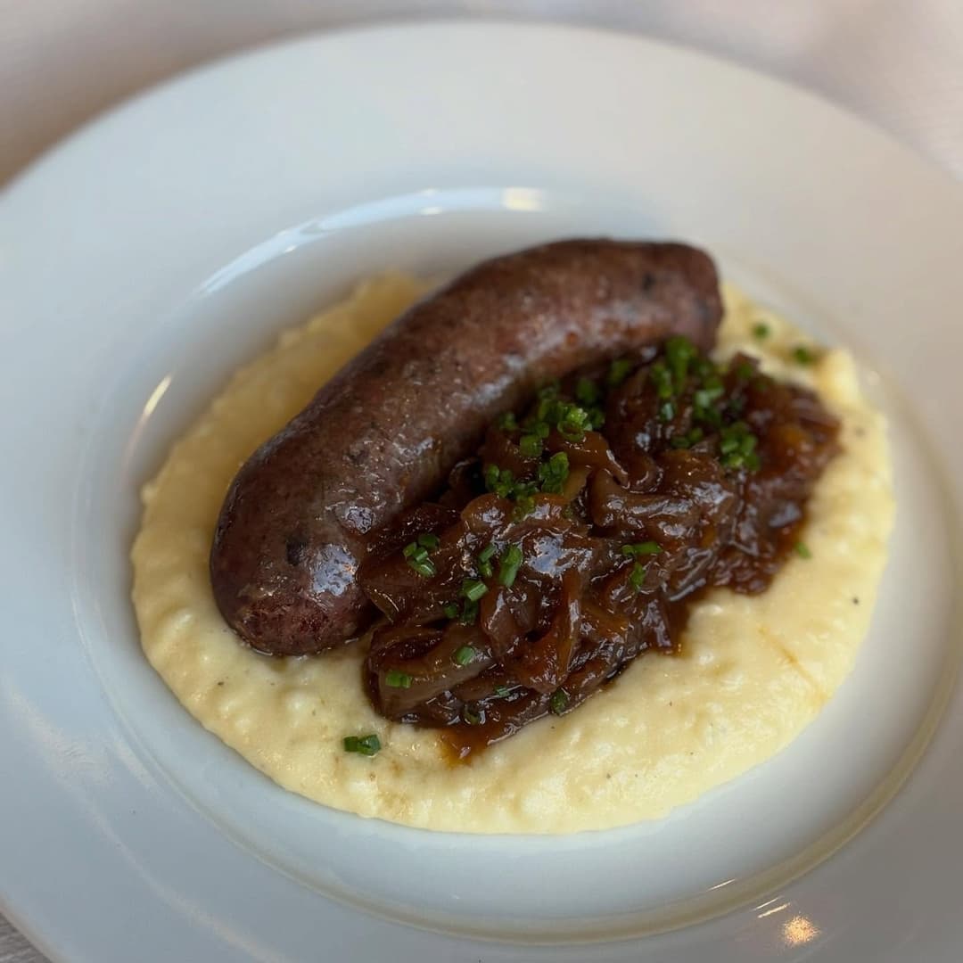 Savory sausage atop creamy polenta, garnished with caramelized onions and fresh chives, exuding a warm, inviting atmosphere.