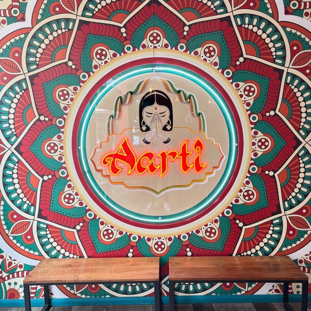 Aarti Indian Restaurant entrance with neon Aarti sign set against floor-to-ceiling mandala mural