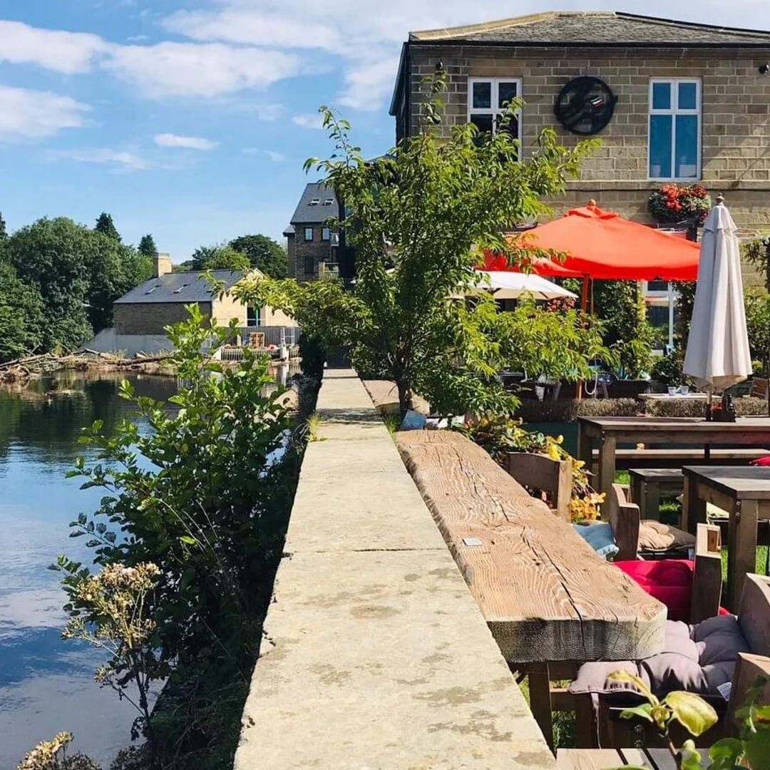 Buon Apps River Lounge — sunny riverside terrace with parasols and the stone building