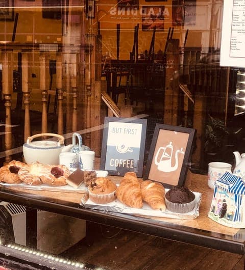 Window display at Chichini showing fresh croissants, muffins, and a But First Coffee sign