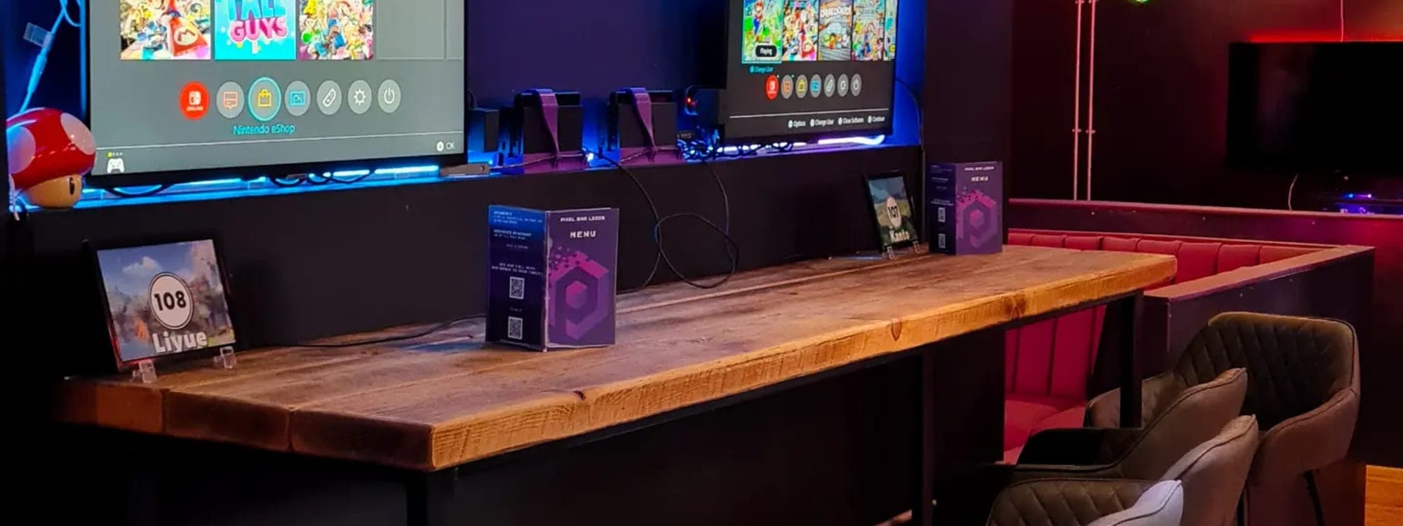 Interior of Pixel Bar Leeds showing gaming booths with multiple screens, blue LED lighting and wooden counter