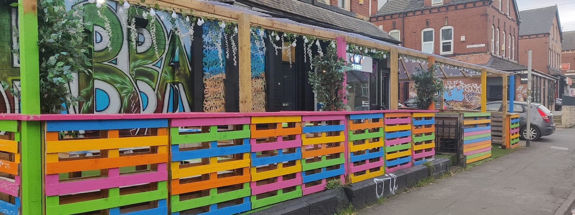 Colourful exterior of Chef Shabbas Kitchen and Cocktails in Hyde Park Leeds with rainbow pallet fence and fairy lights
