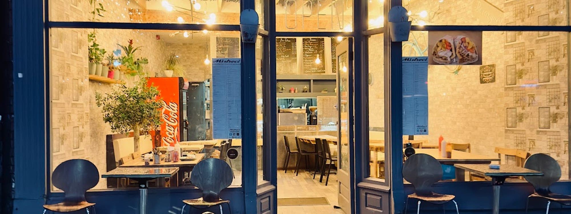 Evening exterior of Mistreci Greek food cafe on The Crescent Hyde Park Leeds with blue lighting and outdoor seating