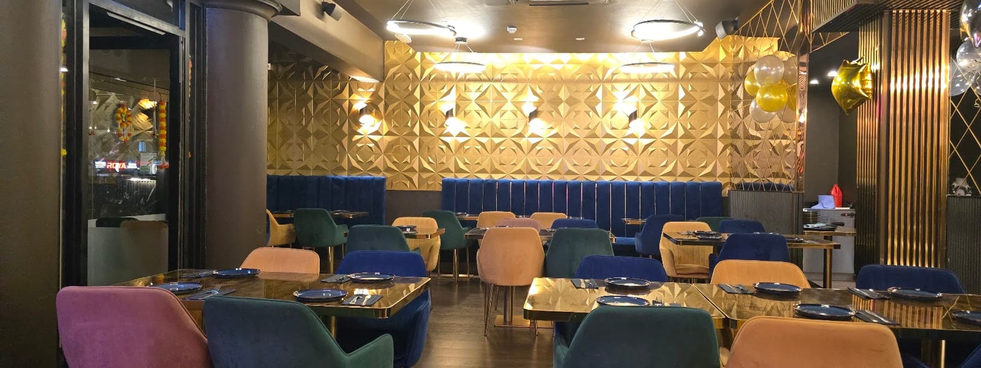 Interior of Mojo Royal Treat restaurant with blue and pink velvet chairs, gold tile wall, and moody lighting