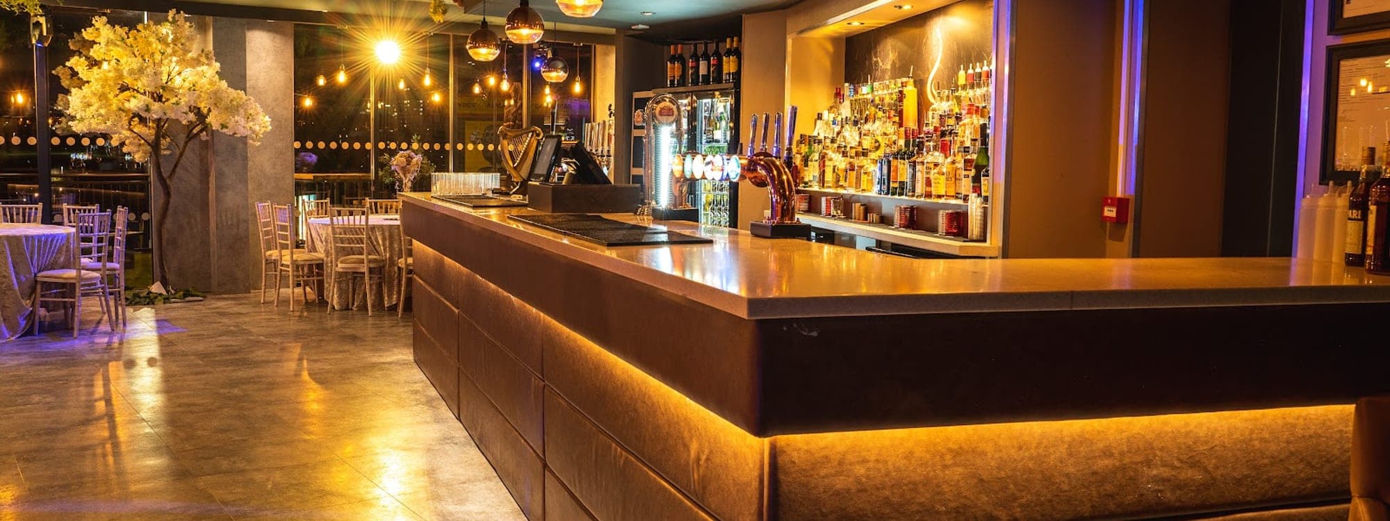 Interior of Sheepscar Bar and Grill with amber-lit bar counter, blossom tree decor, and pendant lighting