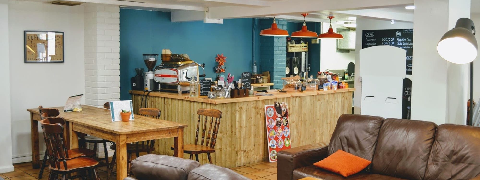 Interior of The Barn Coffee Shop with wooden counter, leather sofas, teal wall, and pendant lights at Meanwood Valley Urban Farm